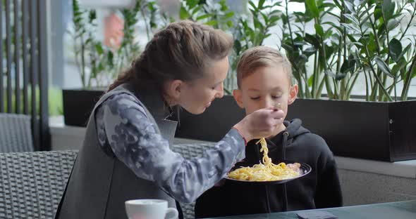 Mom Feeds Pasta To Her Child In A Cafe