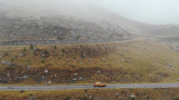 Aerial Shot of Orange Car Riding Through Mountain Road at Autumn