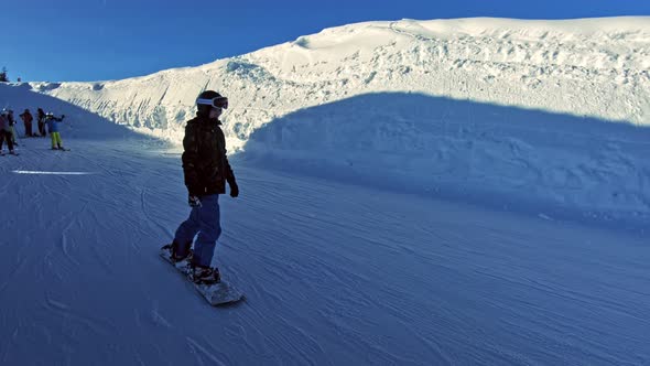 A teenage boy on a snowboard sliding by slowly.