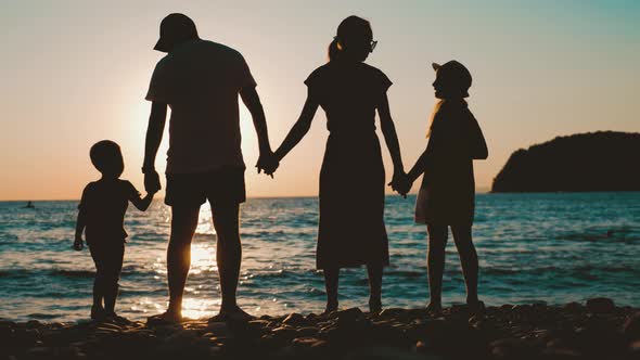 Happy Young Family Together with Children at Sunset. People Silhouettes on Beach. Concept of