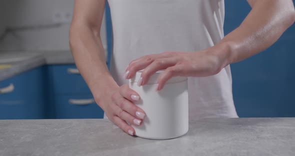 Female Hand Grabs White Jar and Unscrews Lid on It