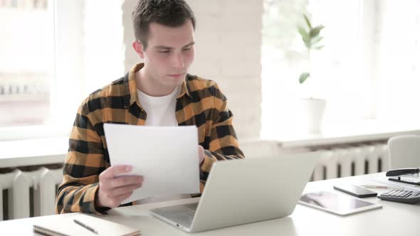 Casual Young Man Doing Paperwork and Typing on Laptop