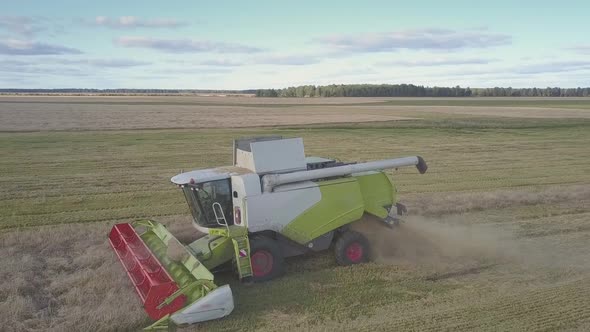 Drone Flies in Front of Huge Harvester Driving on Field