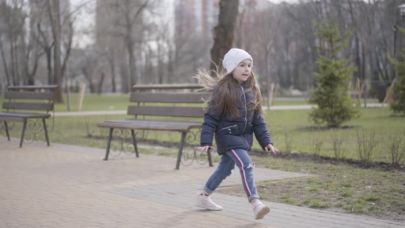 Wide Shot of Joyful Kid Having Fun in Park on Sunny Day. Cheerful Caucasian Little Girl Running and