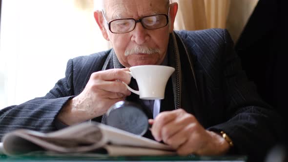 Grayhaired Grandfather is Sitting in a Cafe Drinking Tea He is Reading a Newspaper