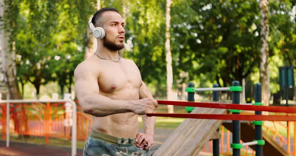 Sportsman Doing Exercises with Resistance Band in Nature Listening to Music with Wireless Headphones