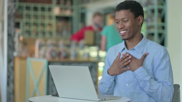 Cheerful African Man Doing Video Call on Laptop in Cafe