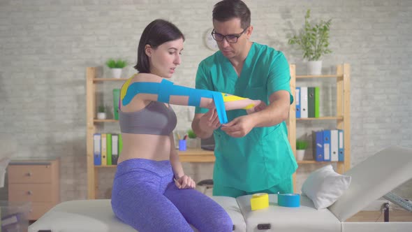 Physical Therapist in Uniform Sticks a Special Kinesiotape on the Patient's Hand