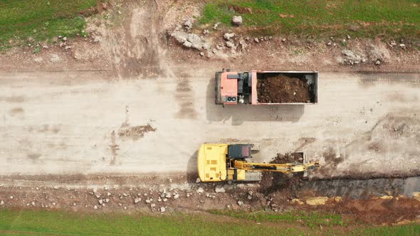 Aerial View of Excavator Loading a Dump Truck with Soil in the Green Field