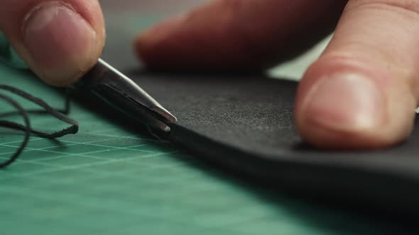 Man Hands Cutting Thin Line on Black Leather with Sharp Knife Closeup
