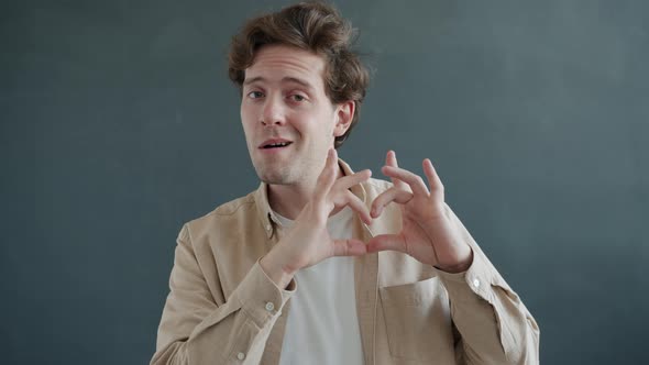 Slow Motion Portrait of Happy Handsome Guy Making Heart Symbol with Fingers Smiling Looking 