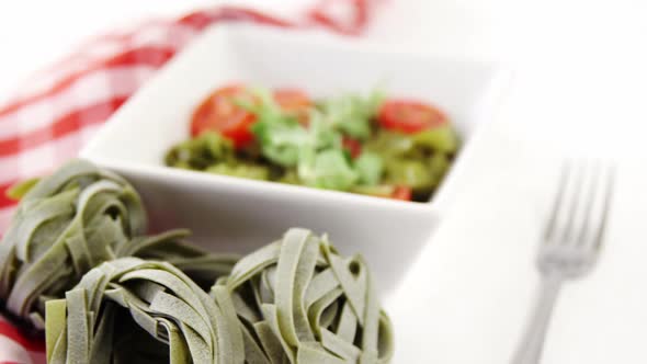 Fresh spinach fettuccine noodles and bowl of salad on table