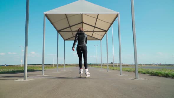 Athletic young woman riding the rollers in black tight leggings flat asphalt road a clear Sunny day