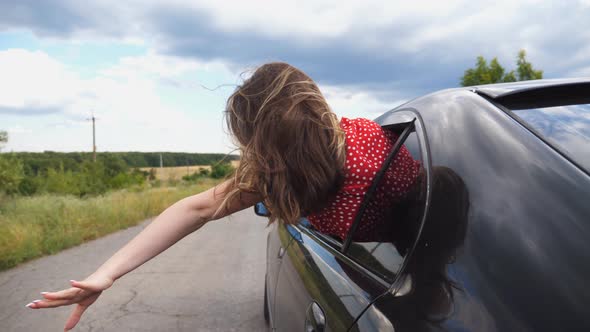 Young Woman Leaning Out of Car Window and Holding Her Hand Out While Riding Through Country Road