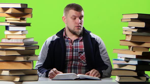 Man Sitting at His Desk Leafing Through a Textbook. Green Screen