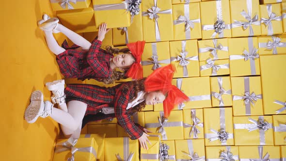 Cute Caucasian Mother and Daughter Dressed in Bright Clothes with a Bow Pose Near Bright Yellow Gift