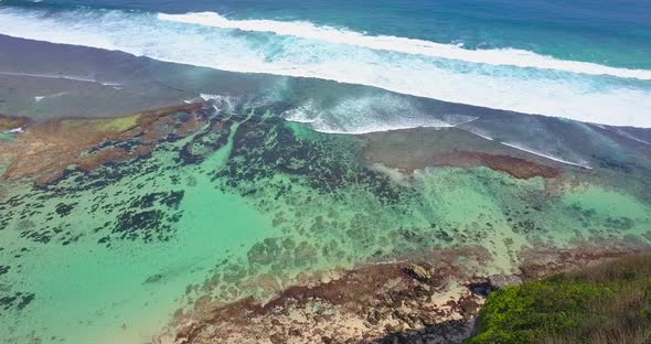 Aerial drone view of a coral reef and waves at the beach.