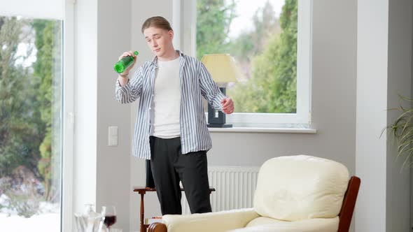 Wide Shot Portrait of Drunk Caucasian Young Man Standing Indoors with Empty Beer Bottle