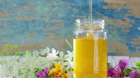 A Stream of Fresh Honey Flows Down in Glass Jar on the Rustic Background
