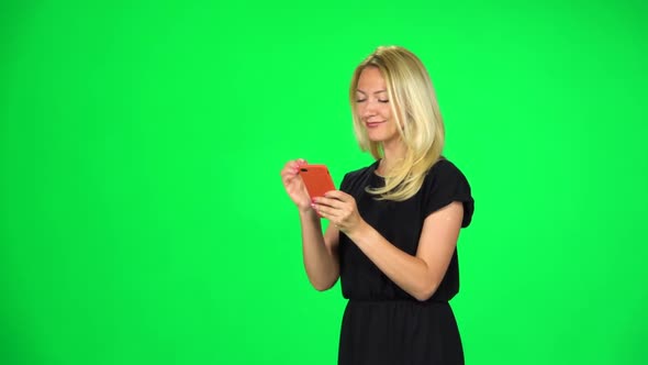 Blonde Woman Goes and Texting with Smartphone on Green Screen at Studio, Slow Motion