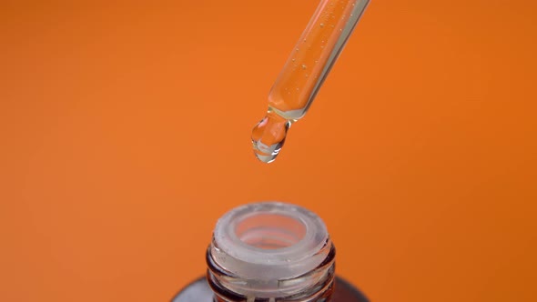 Dropper with a liquid drop in a glass cosmetic bottle on an orange background