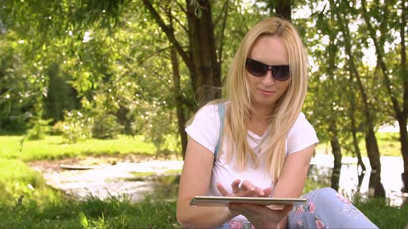 Young Woman Sitting in Park with Tablet Computer, Slow Motion.