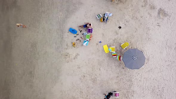 Aerial top down shot of families and couples relaxing on a sandy beach. Dolly out