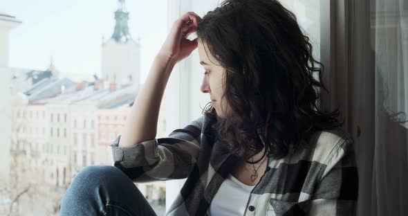 Young Woman Sitting on Window Sill and Enjoying Old Town View