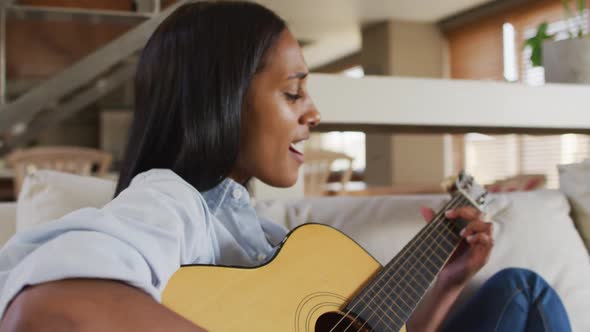 Mixed race woman on couch at home playing guitar and singing