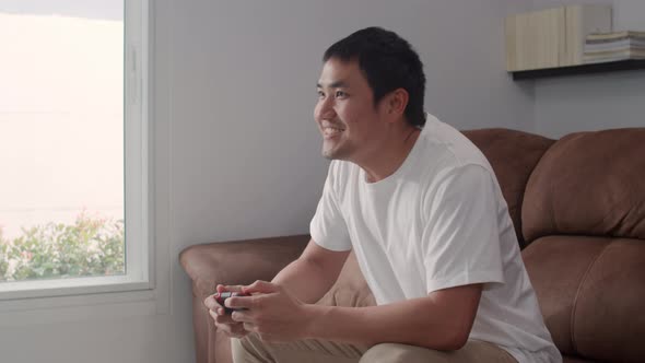 Young Asian man using joystick playing video games in television in living room