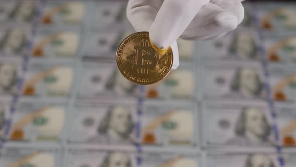 A Hand in White Gloves Holds a Golden Bitcoin on the Background of Dollar Bills