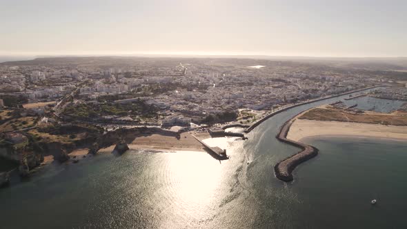 High descending aerial towards the coastline of Lagos in Portugal while a boat is leaving the harbor