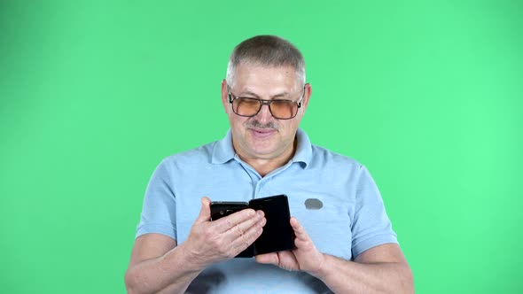 Portrait of Aged Man Talking for Video Chat Using Mobile Phone,, Isolated Over Green Background.