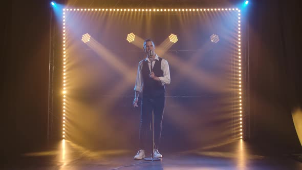 A Young Stylish Guy Vocalist Singing and Gestures with His Hands on Stage in a Vintage Microphone