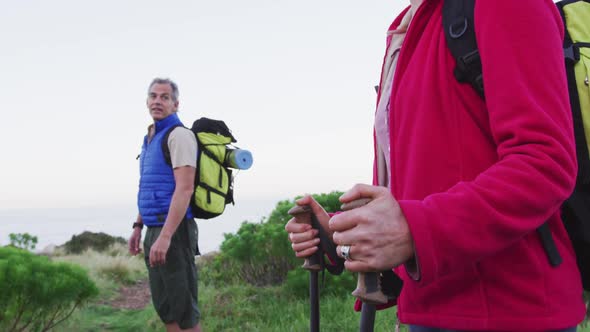Senior hiker couple with backpacks and hiking poles looking at each other standing