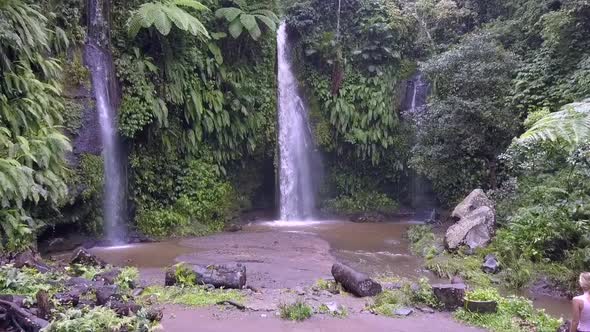 Lonely blonde girl walking to waterfall.Fantastic aerial view flight fly forwards drone footage Ben