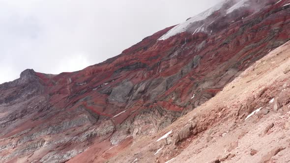 Aerial view, flying over a slope with red and grey colored slopes of a vulcano in the background 