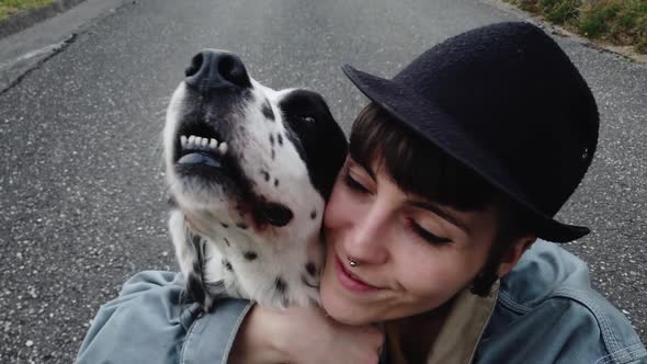 Positive young lady playing with dog while sitting on ground on street