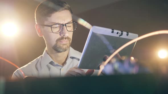 A Man in Glasses Is Operating a Tablet While Observing a 3D-printer