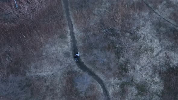 A top down view directly above two people walking on a dirt path in a park during a cloudy evening.