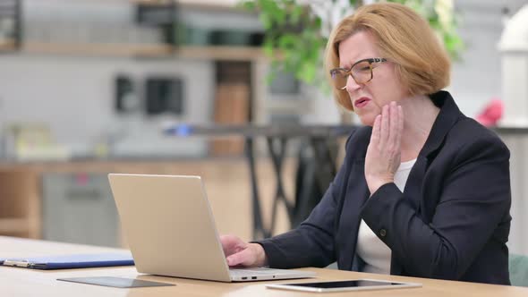 Old Businesswoman with Laptop Having Toothache in Office