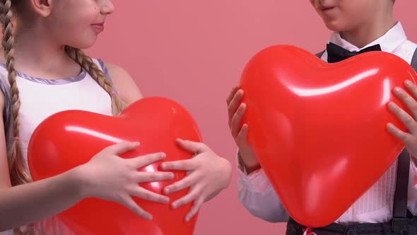 Cheerful Little Couple Holding Heart-Shaped Balloons and Smiling to Camera, Love