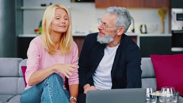 Adult Man and Woman are Sitting on a Cozy Sofa Choosing a Movie to Watch Together