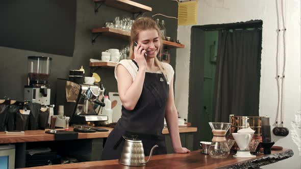 Young Female Coffe Shop Owner Have a Phone Call Using Smartphone in Cafeteria