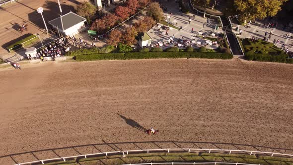 A dynamic tracking aerial footage of trotting horses to their starting point while ridden by jockeys