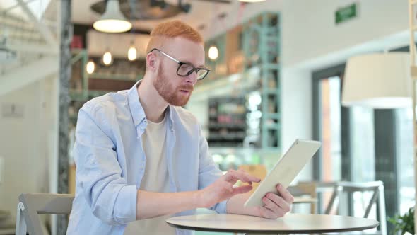 Redhead Man Celebrating Success on Tablet in Cafe 