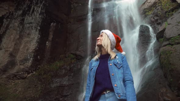 girl in Santa Claus hat stands on waterfall on Christmas Day. Enjoying nature