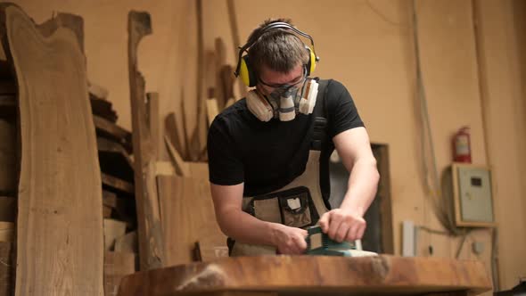 Wood craftsman grinds a piece of wood for a table in a workshop