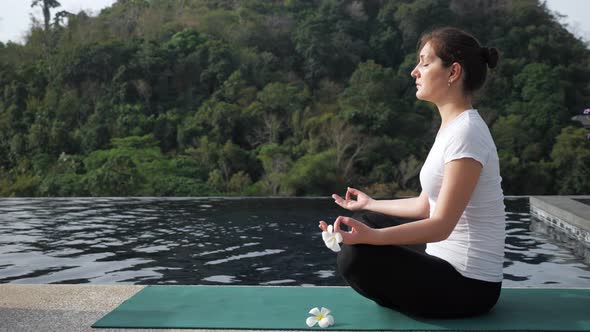 Young Woman Sits in a Lotus Position Near the Rooftop Pool