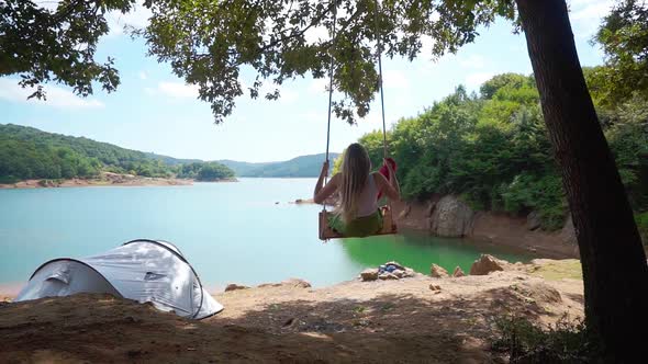 Young Woman Swinging Near Lake Camp Side In Summer 2